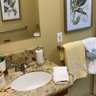 A neatly organized bathroom with a granite countertop, featuring a sink, towels, and decorative artwork on the wall.