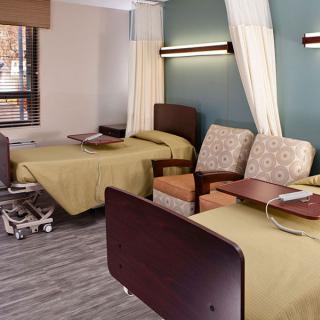 A hospital room with two beds, chairs, and privacy curtains.