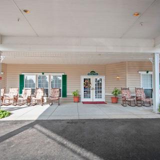 The exterior entrance of a building featuring chairs and potted plants under a covered walkway.