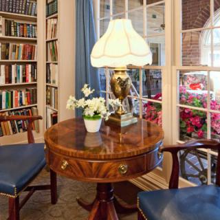 A cozy library nook with a round table, lamp, and bookshelves.