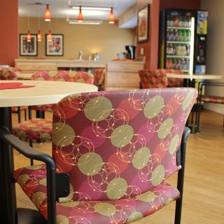 A cozy cafe interior with patterned chairs and tables, featuring a vending machine in the background.