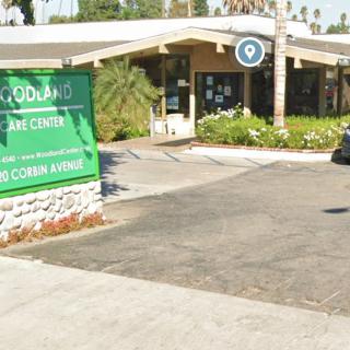 A building with a green sign and a parking lot in front, surrounded by trees.