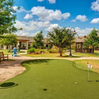 A well-maintained outdoor mini golf course on a sunny day, featuring a putting green and surrounding benches.