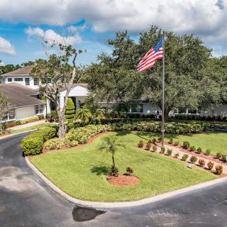 A building with a landscaped entrance, featuring an American flag and surrounded by trees and greenery.