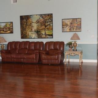 A cozy living room featuring a brown leather sofa, decorative paintings on the wall, and elegant lamps on side tables.