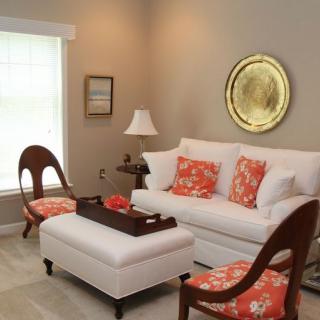 A modern living room featuring a white sofa and ottoman, complemented by wooden armchairs with vibrant orange cushions.