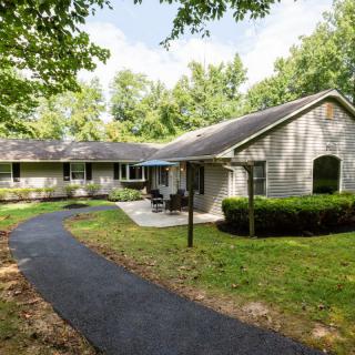 A single-story house with a well-maintained lawn and a curved driveway surrounded by trees.