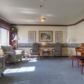 A cozy living room featuring comfortable chairs, a piano, and decorative artwork on the walls.