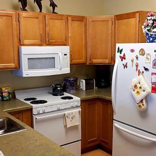 A cozy kitchen with wooden cabinets, featuring a microwave, stove, and refrigerator decorated with magnets.