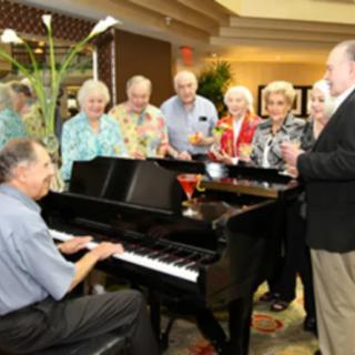 A group of people enjoying a musical performance around a piano indoors.