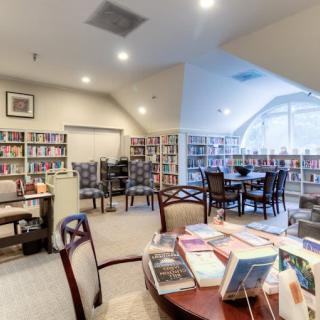 A cozy library reading area with bookshelves, tables, and chairs.