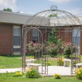 A metal gazebo surrounded by greenery and benches in a garden setting.