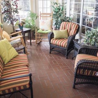A cozy sunroom with wicker furniture and striped cushions surrounded by plants.