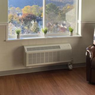 A cozy room with a window view, featuring small plants and a wall-mounted heater.