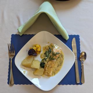 A neatly arranged plate of food with vegetables and sauce, accompanied by cutlery on a table setting.