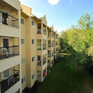 A view of a residential apartment building with multiple balconies and surrounding greenery on a sunny day.