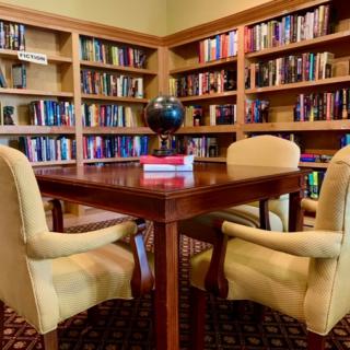 A cozy library corner with bookshelves and a wooden table surrounded by chairs.
