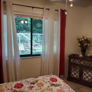 A cozy bedroom featuring a floral bedspread, sheer curtains, and a garden view through the window.