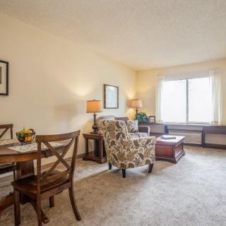 A cozy living room with a dining area, featuring comfortable seating and natural light from a large window.