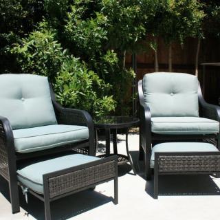A cozy patio setup featuring two cushioned chairs with footrests and a small table, surrounded by greenery.