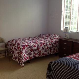 A cozy bedroom with two beds, a small lamp on a side table, and natural light filtering through the window.
