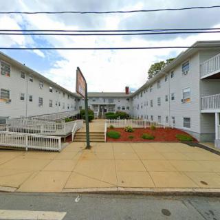 An exterior view of a multi-story apartment building with a paved walkway and landscaped courtyard.