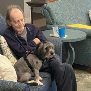 An elderly man sitting on a couch with a dog on his lap.