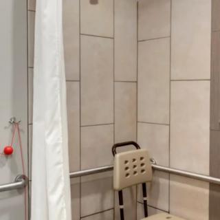 An accessible bathroom with a shower chair and grab bars for safety.