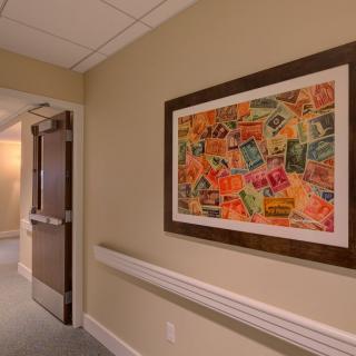A hallway with a colorful abstract painting on the wall, next to an open door.