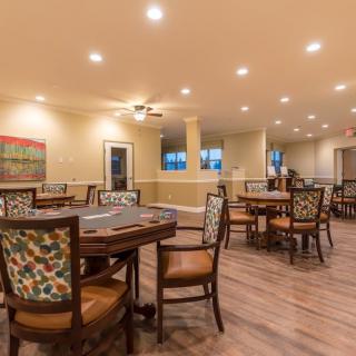 A spacious and well-lit dining area with multiple tables and chairs, featuring a wooden floor and ceiling lights.