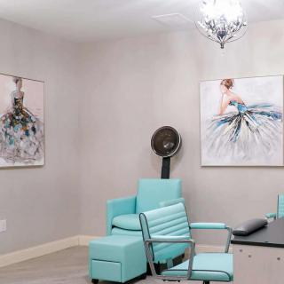 A modern salon room with turquoise furniture, featuring a hair dryer and elegant artwork on the walls.