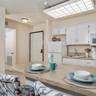 A modern kitchen in an apartment featuring white cabinets, a central countertop with place settings, and bar stools.