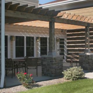 A patio with a pergola and stone columns, featuring outdoor seating and surrounding landscaping.