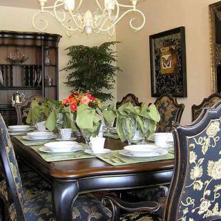 An elegantly decorated dining room featuring a large table set with plates and surrounded by ornate chairs, complemented by a sophisticated chandelier and decorative plants.