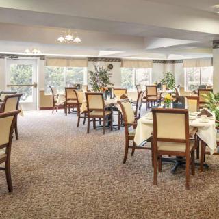 A spacious and elegantly decorated dining room with several tables and chairs, featuring large windows and a carpeted floor.