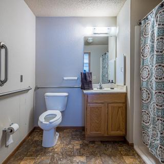A clean and modern bathroom featuring a toilet, sink with a wooden cabinet, and a shower with a patterned curtain.