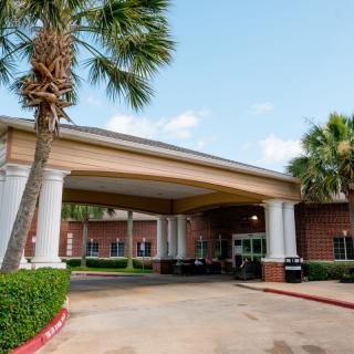 Entrance of a building with a covered walkway and palm trees.
