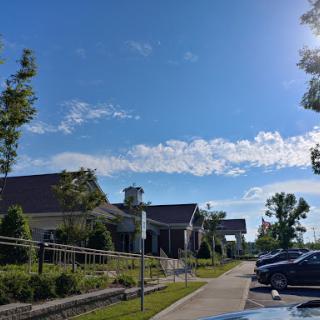 A clear day with a blue sky and puffy clouds over a well-maintained building and parking area.