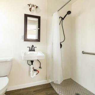 A modern bathroom with a wall-mounted sink, mirror, and walk-in shower featuring black fixtures.