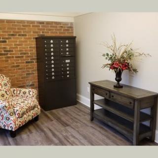 A cozy corner with a patterned chair, wooden table holding a floral arrangement, and a brick accent wall.