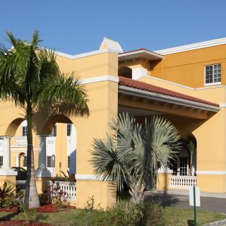 A sunny view of a hotel building with palm trees and landscaped gardens.