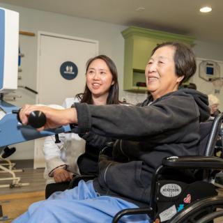 An elderly person in a wheelchair participating in a therapy session with assistance.