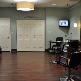 A modern hair salon interior featuring chairs, a television, and stylish lighting.
