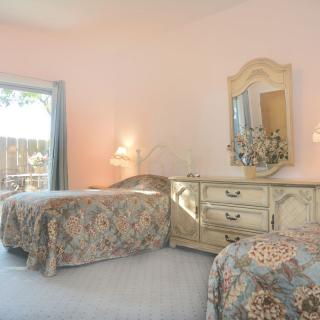 A cozy bedroom with twin beds featuring vintage furniture and floral bedding, illuminated by natural light.