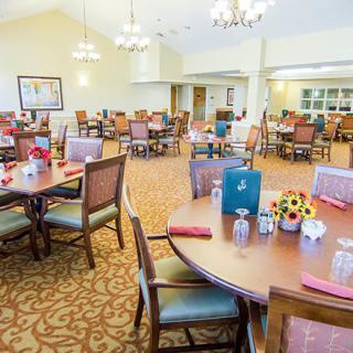 A spacious dining room with neatly arranged tables and chairs, featuring elegant chandeliers and warm decor.