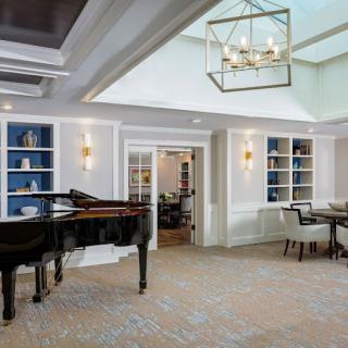 A modern interior room featuring a grand piano, elegant chandelier, and built-in shelves.