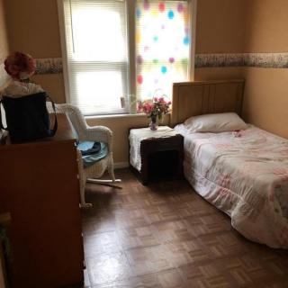 A cozy single bedroom with wooden flooring and simple furnishings.