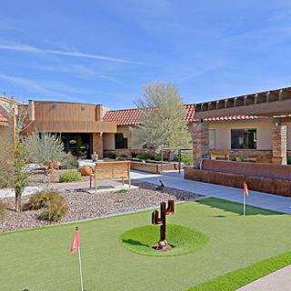 A serene outdoor recreational area featuring a putting green surrounded by modern architecture and lush landscaping under a clear blue sky.