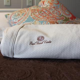 A neatly rolled towel featuring embroidered branding, resting on a stylish bed with patterned pillows.