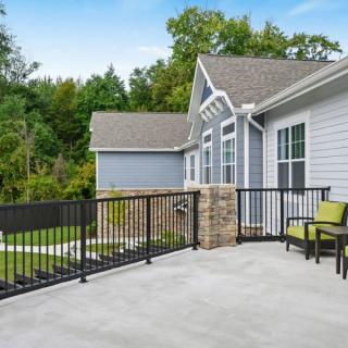 A modern house with a spacious patio featuring outdoor seating and railings, surrounded by lush greenery.